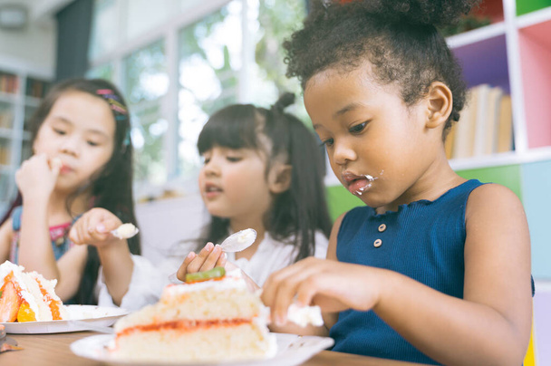 cute little child girl with diversity friends eating cake together. kids eat dessert .  - Foto, imagen