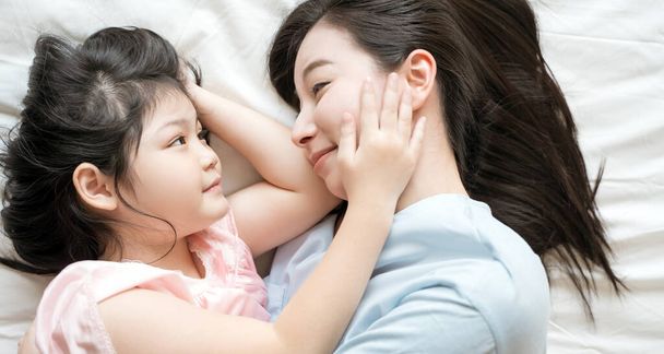 Мать и дочь девочка проводят время вместе в спальне Взгляните друг на друга и улыбнитесь.
 - Фото, изображение