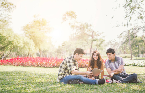 happy students sitting and tutoring with tablet screen each other in a campus at park with a warm light - Foto, Imagen