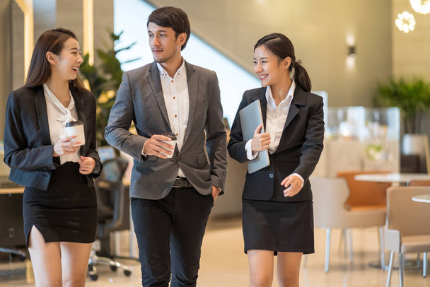 Ázsiai üzletemberek sétálnak be az irodaházba. Fiatal üzletember és üzletasszony beszél séta közben. - Fotó, kép