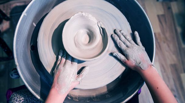 τα χέρια των νέων καλλιτεχνών διαμόρφωση πηλό στον τροχό αγγειοπλαστικής στο Εργαστήρι κεραμικών στούντιο - Φωτογραφία, εικόνα