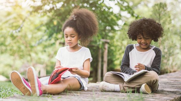 little Afro child girl reading book between green spikes meadow garden with friend  read education concept - Фото, зображення
