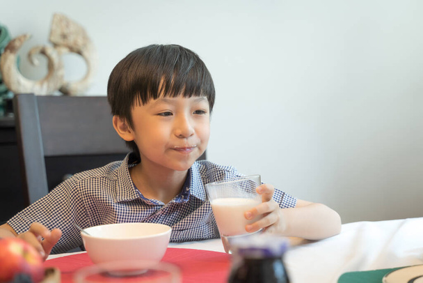 The boy is eating milk and breakfast at home. - Fotografie, Obrázek