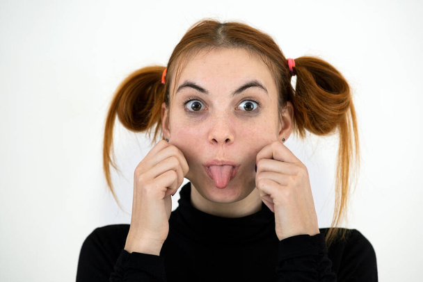 Nahaufnahme Porträt eines lustigen rothaarigen Teenagers mit kindischer Frisur, die ihre Zunge isoliert auf weißem Hintergrund ausstreckt. - Foto, Bild