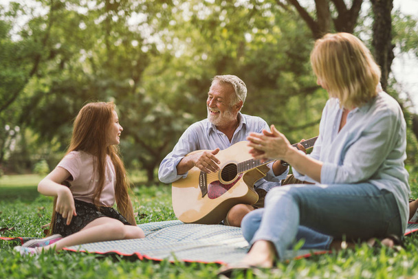 family enjoying quality time, playing guitar in their green park garden. - Fotó, kép