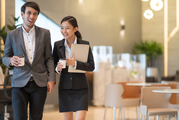 Asian business people  walking in office building. Young businessman and businesswoman talking when walking. - Zdjęcie, obraz