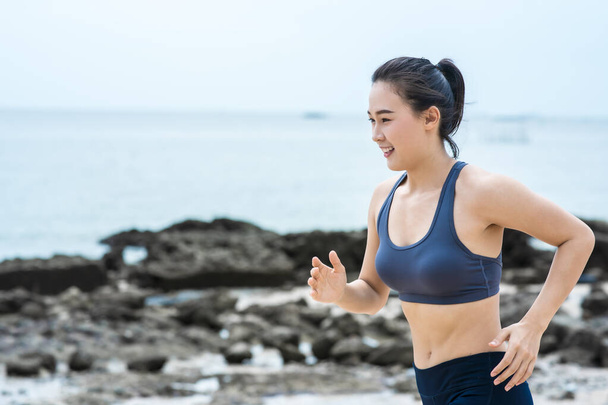 Young Asian woman running on the beach. Girl jogging workout in seaside - Fotó, kép