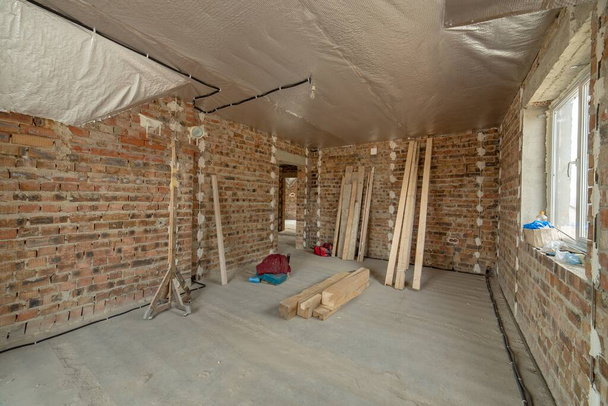 Interieur van onafgewerkte bakstenen huis met betonnen vloer en kale muren klaar voor pleisterwerk in aanbouw. Ontwikkeling van onroerend goed - Foto, afbeelding