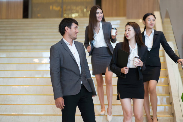 Ázsiai üzletemberek sétálnak be az irodaházba. Fiatal üzletember és üzletasszony beszél séta közben. - Fotó, kép