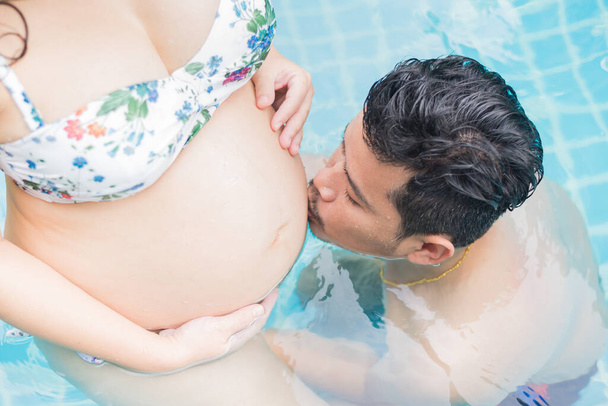 Aasian raskaana oleva nainen, jolla on iso vatsa. Rentoudu ja liikunta uima-altaalla miehensä kanssa. - Valokuva, kuva