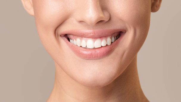 Unerkennbare Frau mit weißen Zähnen posiert lächelnd auf beigem Hintergrund - Foto, Bild