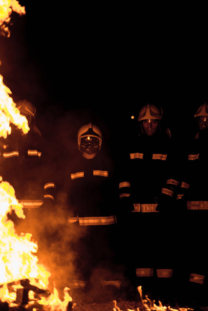 Feuerwehr-Team in Uniform mit Schutzhelmen löscht Brand in der Gegend - Foto, Bild