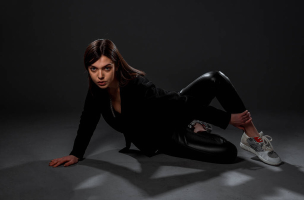 Houkutteleva nuori nainen malli poseeraa tyylikäs musta lateksi housut, top ja lenkkarit - Valokuva, kuva