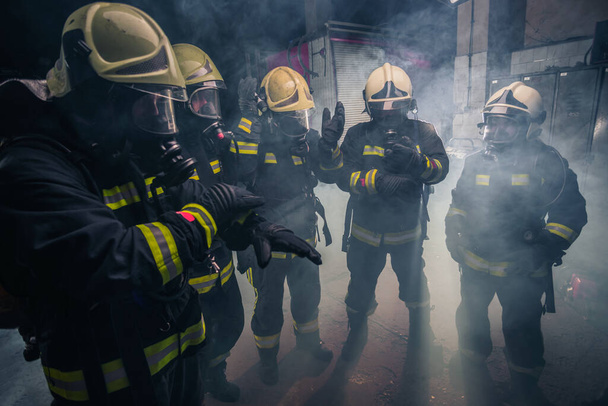 Firemen in uniform wearing gloves and gas masks inside the fire department - Photo, Image