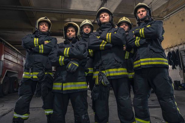 Grupo de bomberos de pie confiados con los brazos cruzados. Bomberos listos para el servicio de emergencia. - Foto, imagen