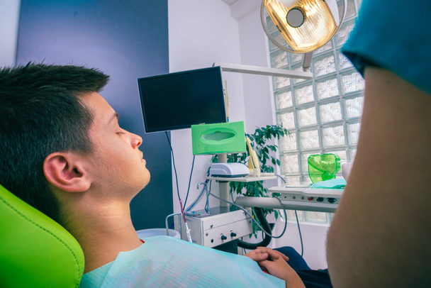 Adolescent assis comme patient dans une chaise de dentiste et dentiste masculin le préparant pour un contrôle régulier - Photo, image
