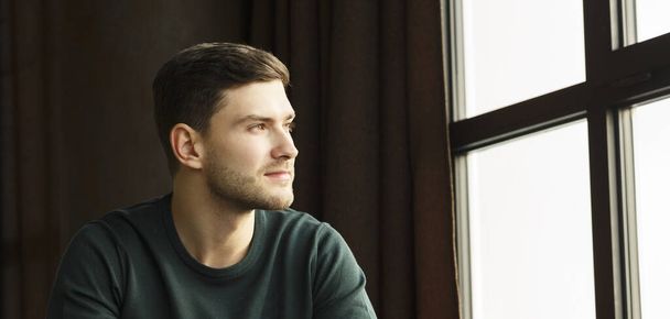 Jeune homme regardant à l'extérieur assis près de la fenêtre Intérieur
 - Photo, image