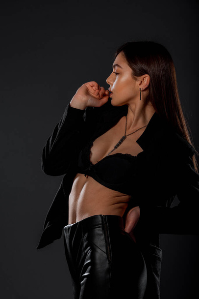 Body shot of a cool modern girl wearing black top and black leather pants - Fotó, kép