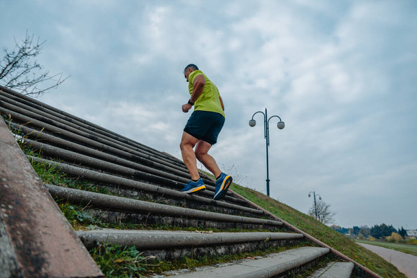 Idősebb férfi futó aktív ruhába öltözve futógyakorlatot végez a lépcsőn. - Fotó, kép