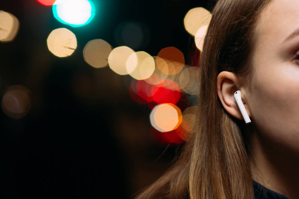 girls ear in which the earphone against the background of the city. Girl in AirPods. Copy space. Night city - Photo, image