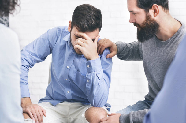 Huolestuneet potilaat lohduttavat järkyttynyt mies ryhmäterapiassa istuntoon rehab
 - Valokuva, kuva