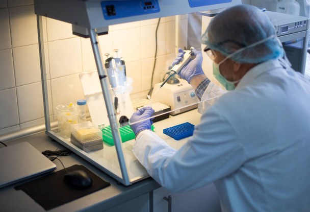 Biólogo com equipamento de proteção trabalhando em amostras em caixa de luva de isolamento uv em laboratório
 - Foto, Imagem