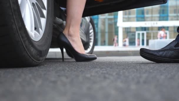 Businessman opens and holds door of car for beautiful young woman. Slim legs of businesswoman in shoes on high heels getting out of auto. Close up Slow motion Low angle view - Footage, Video
