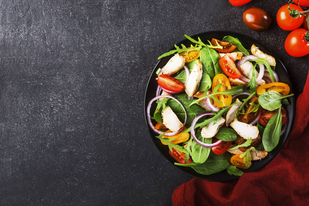 Spring salad with spinach, grilled chicken, cherry tomatoes, arugula, corn salad and red onion. Healthy food concept. Black stone table. Top view. Copy space - Photo, Image
