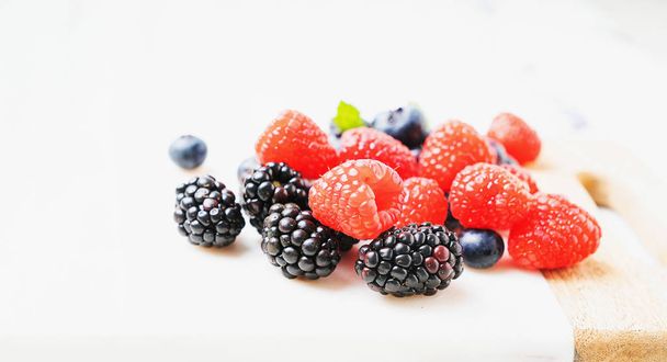 Ripe and juicy fresh berries on the marble wooden board backgrounds. Blueberry, Raspberry and Blackberry. Side view. Selective focus. - Photo, Image