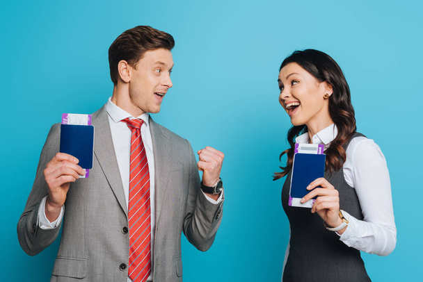two happy businesspeople looking at each other while holding passports and air tickets on blue background - Foto, afbeelding