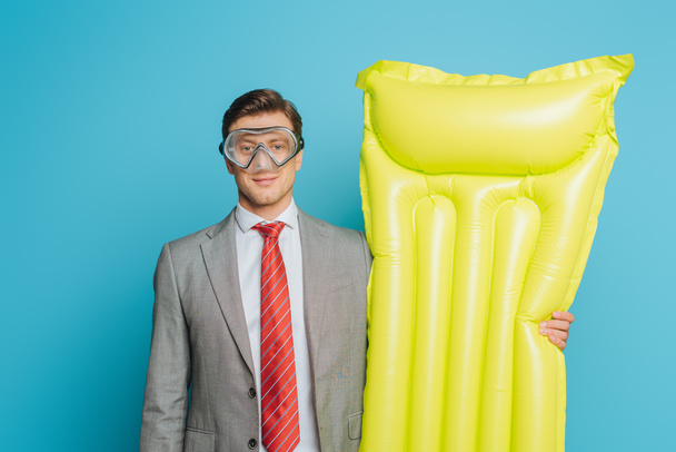 smiling businessman in diving mask holding inflatable mattress on blue background - Foto, imagen