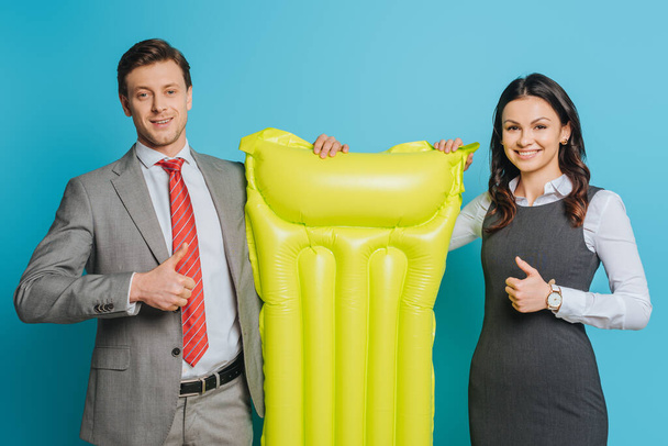 two happy businesspeople holding yellow inflatable mattress and showing thumbs up on blue background - Photo, Image