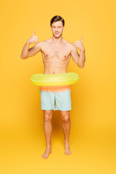 smiling man in swim ring showing thumb up while looking at camera on yellow background - Photo, Image