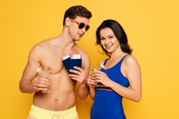 happy couple with glasses of cocktail, passports and air tickets on yellow background - 写真・画像