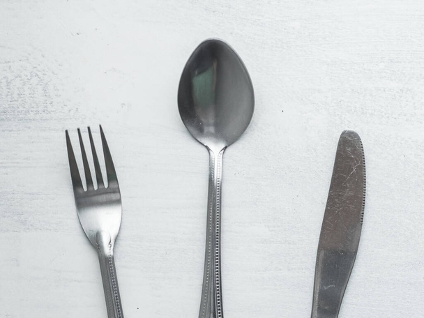 Ensemble de fourchettes, cuillères et couteaux mélangés sur un fond blanc grossièrement peint
 - Photo, image