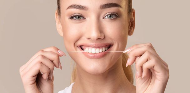 Hymyilevä nainen käyttäen Floss puhdistus hampaat poseeraa yli Beige tausta
 - Valokuva, kuva