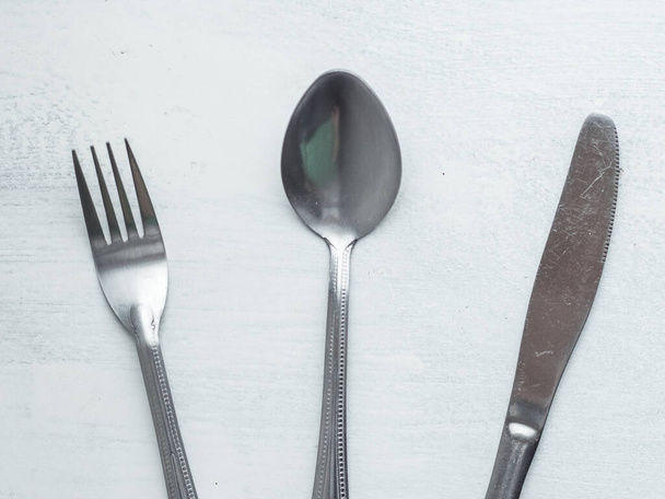 Ensemble de fourchettes, cuillères et couteaux mélangés sur un fond blanc grossièrement peint
 - Photo, image