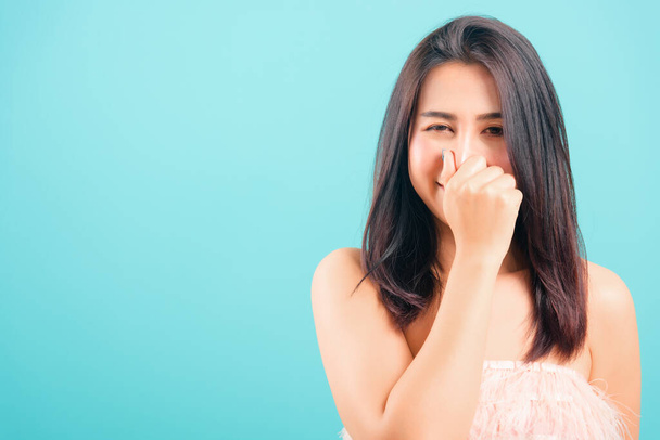 Smiling face Asian beautiful woman use hand holding her nose because of bad smell on blue background, with copy space for text - Photo, Image