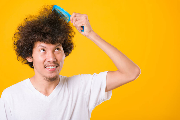 Asian man combing curly hair on yellow background with copy space for text - Zdjęcie, obraz