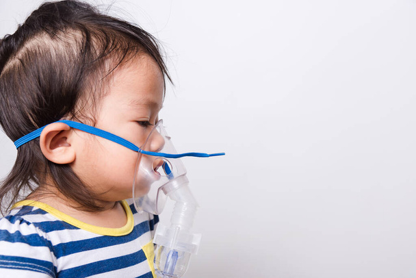 Closeup Asian face, Little baby girl sick her using steam inhaler nebulizer mask inhalation oneself on white background with copy space, health medical care - Valokuva, kuva