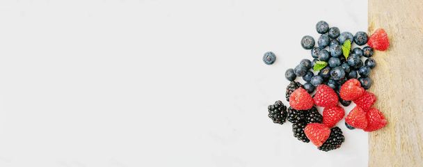 Reife und saftige frische Beeren auf den Hintergründen des Marmorbretts. Blaubeere, Himbeere und Brombeere. Ansicht von oben. Banner - Foto, Bild
