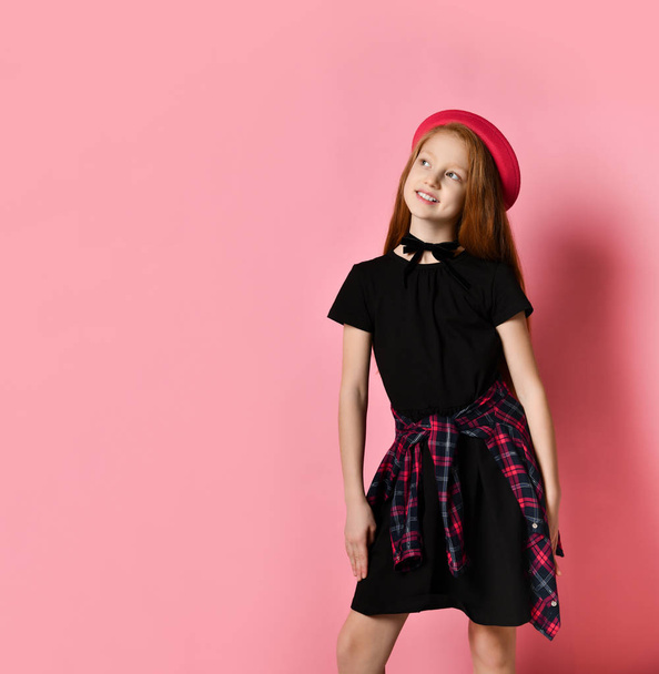 Ginger teenage girl in black dress, checkered shirt on waist, red hat and choker. She smiling, posing on pink background. Close up - Foto, imagen