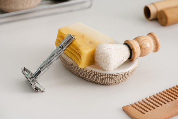Nahaufnahme von Schale mit Seife, Rasierpinsel und Rasiermesser in der Nähe Kamm auf grau, Zero-Waste-Konzept - Foto, Bild