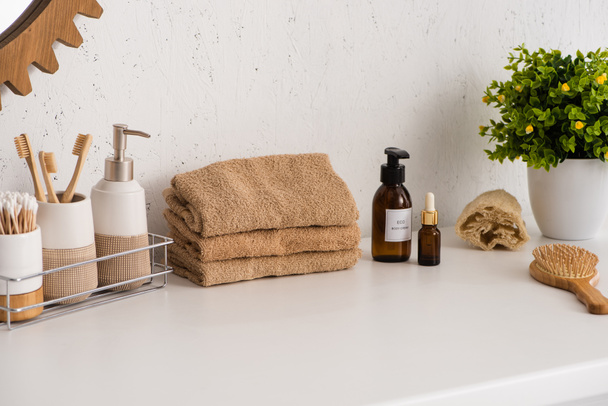 Plank met hygiëne-objecten in de buurt van handdoeken, schoonheidsproducten en bloempot in de badkamer, afvalvrij concept - Foto, afbeelding