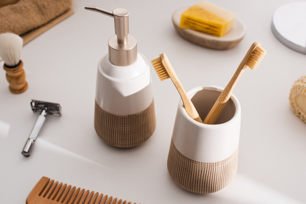 Close up view of liquid soap, toothbrush holder with toothbrushes and hygiene objects on grey, zero waste concept - 写真・画像