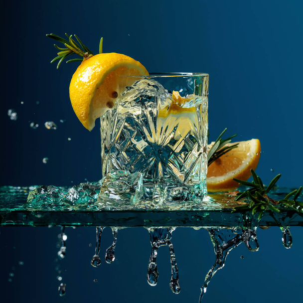 Cóctel gin-tonic con limón y romero. Bebida carbonatada con trozos de hielo en una mesa de vidrio
. - Foto, imagen