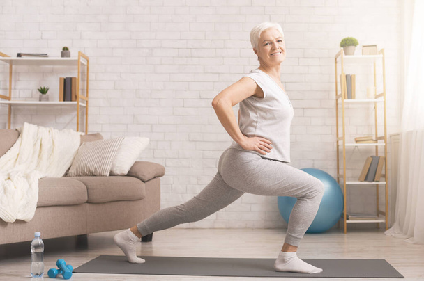 Sporty senior lady doing lunges at home, empty space - Photo, Image
