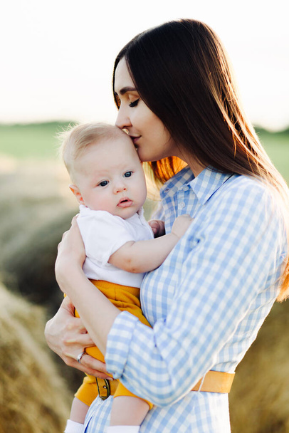 une jeune mère heureuse avec un petit enfant dans ses bras, embrassant doucement sa tête, se tient au milieu d'un champ dans les rayons du soleil couchant
 - Photo, image