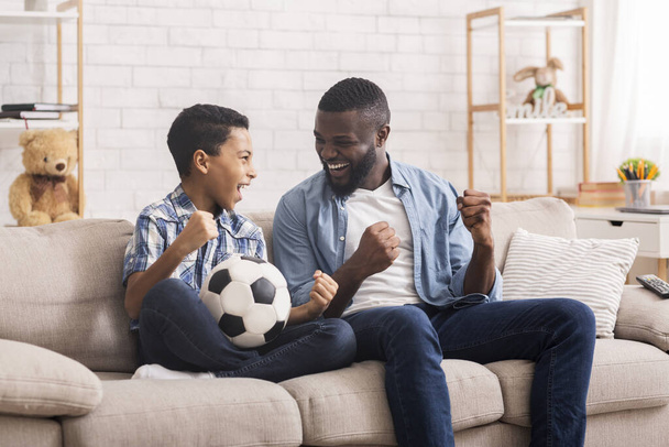 preadolescente negro chico viendo fútbol partido en tv con su padre
 - Foto, Imagen