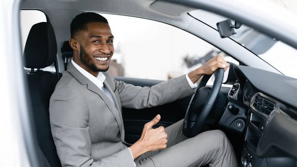 Businessman Buying Car Gesturing Thumbs-Up In Drivers Seat In Showroom - Foto, afbeelding